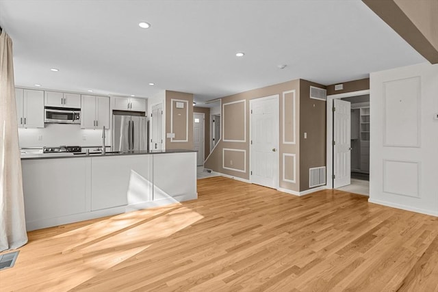 unfurnished living room with visible vents, a sink, baseboards, light wood-style floors, and recessed lighting