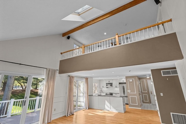 unfurnished living room featuring visible vents, a sink, light wood-style floors, and high vaulted ceiling
