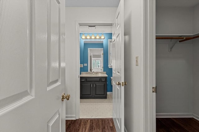 hall featuring baseboards, a sink, and dark wood-style flooring