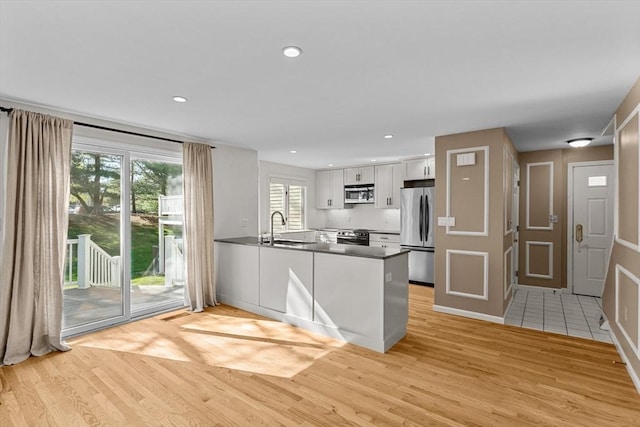 kitchen featuring dark countertops, appliances with stainless steel finishes, a sink, a peninsula, and light wood finished floors