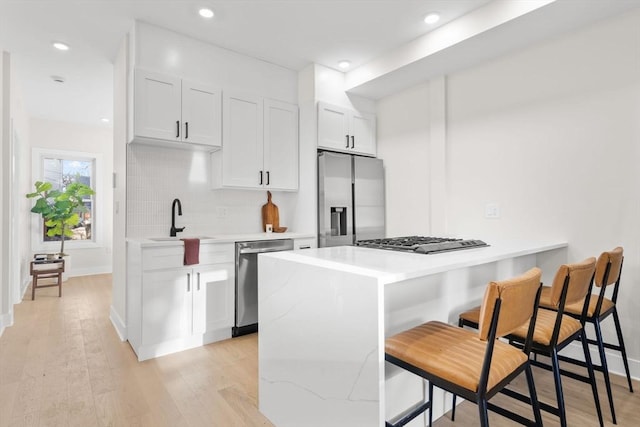 kitchen with a breakfast bar, light wood finished floors, stainless steel appliances, and a sink