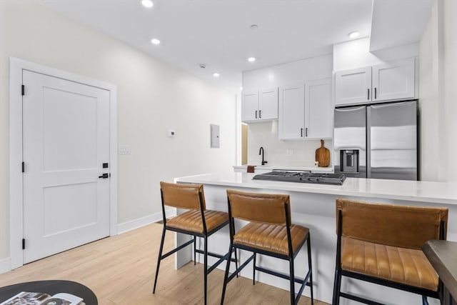 kitchen featuring a kitchen breakfast bar, light countertops, stainless steel refrigerator with ice dispenser, light wood finished floors, and tasteful backsplash