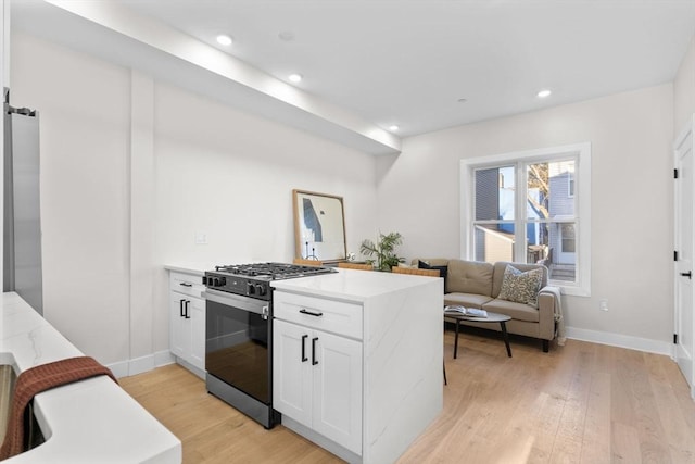 kitchen with a peninsula, light wood-style flooring, gas range, and white cabinetry