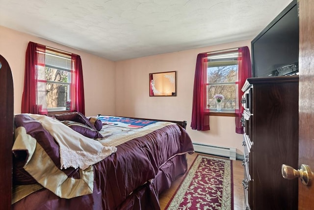 bedroom featuring wood finished floors, a baseboard heating unit, and multiple windows