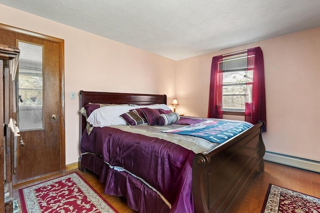 bedroom with baseboards, a baseboard radiator, wood finished floors, and multiple windows