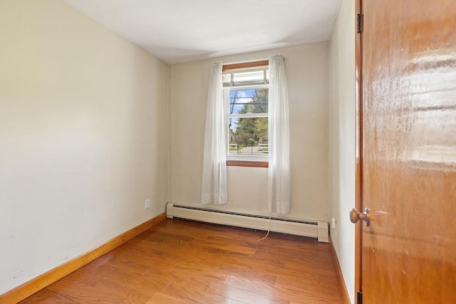 unfurnished room featuring baseboards, a baseboard heating unit, and wood finished floors