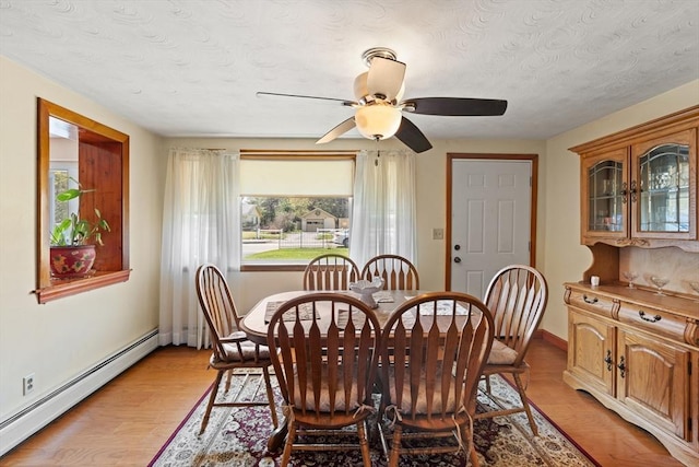 dining room featuring a ceiling fan, a textured ceiling, baseboard heating, baseboards, and light wood-style floors