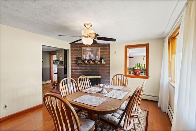 dining area featuring a fireplace, a ceiling fan, wood finished floors, and a baseboard radiator