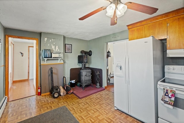 kitchen with a ceiling fan, a wood stove, a baseboard radiator, under cabinet range hood, and white appliances
