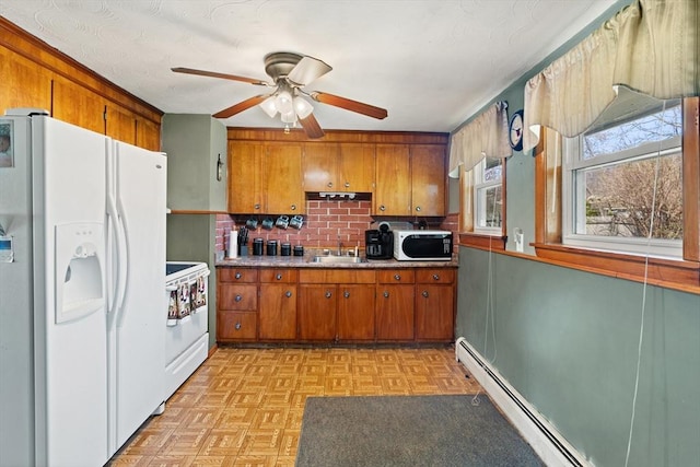 kitchen with brown cabinets, ceiling fan, baseboard heating, a sink, and white appliances