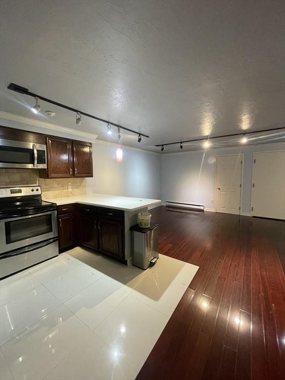 kitchen featuring backsplash, a baseboard heating unit, light wood-type flooring, appliances with stainless steel finishes, and dark brown cabinetry