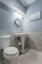 half bathroom featuring tile walls, toilet, and a wainscoted wall