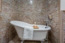 bathroom with a soaking tub and brick wall