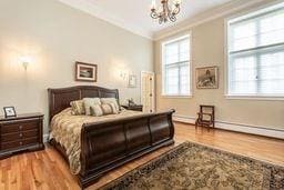 bedroom featuring a notable chandelier, ornamental molding, and wood finished floors