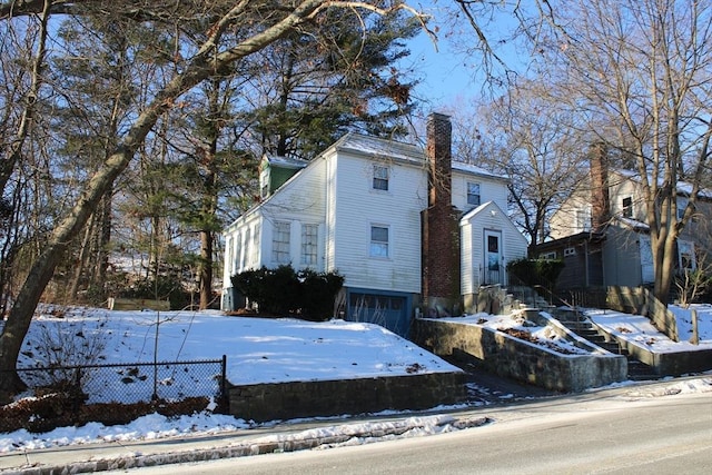 view of snow covered exterior featuring entry steps, a chimney, a garage, and fence