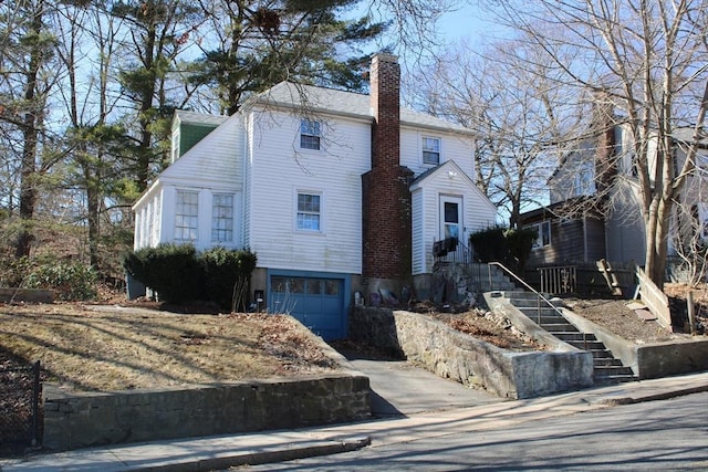 colonial house with an attached garage, driveway, and a chimney