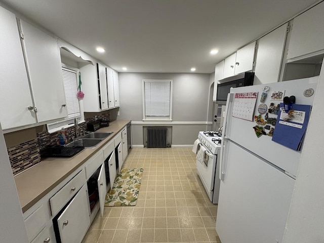 kitchen featuring radiator heating unit, white cabinetry, sink, light tile patterned floors, and white appliances