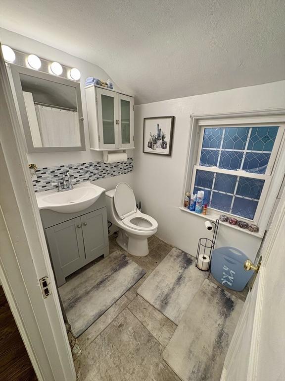 bathroom with vanity, vaulted ceiling, a textured ceiling, and backsplash