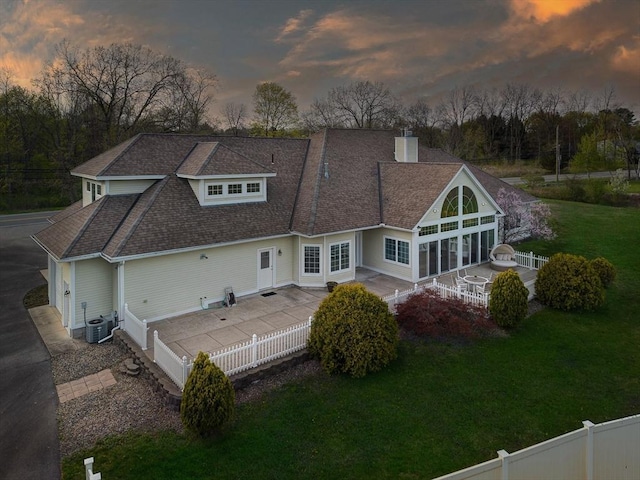 rear view of property with a lawn, a shingled roof, a chimney, and a fenced backyard