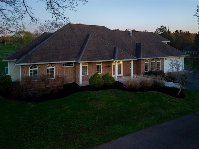 view of front of house featuring brick siding, a shingled roof, and a front lawn