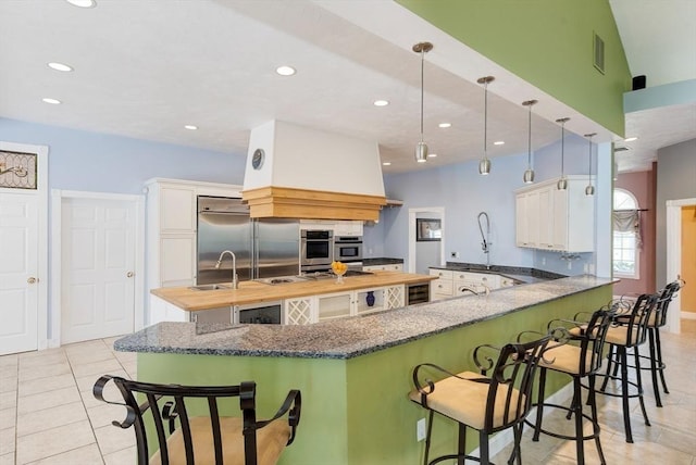 kitchen featuring stainless steel built in fridge, recessed lighting, a peninsula, and an island with sink