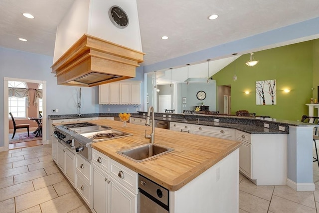 kitchen with a center island with sink, a sink, light tile patterned floors, stainless steel cooktop, and butcher block countertops