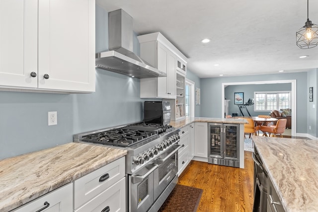 kitchen featuring white cabinets, wine cooler, wood finished floors, wall chimney range hood, and double oven range