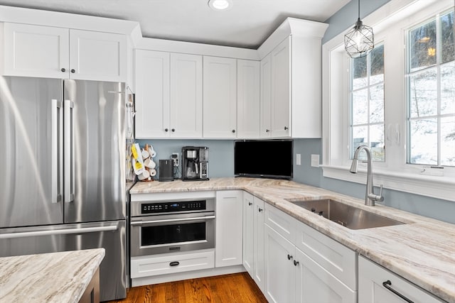 kitchen with stainless steel appliances, white cabinetry, a sink, and light stone counters