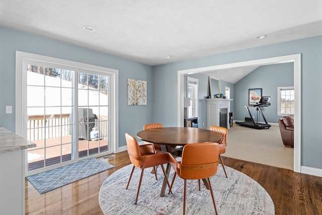 dining room with recessed lighting, a glass covered fireplace, vaulted ceiling, wood finished floors, and baseboards