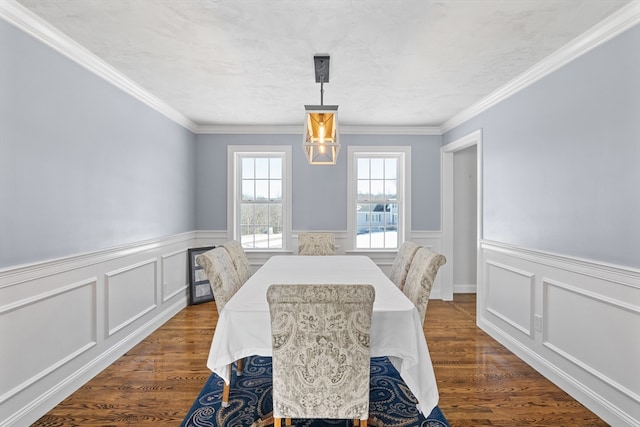 dining room with a wainscoted wall, a decorative wall, dark wood-style flooring, and crown molding