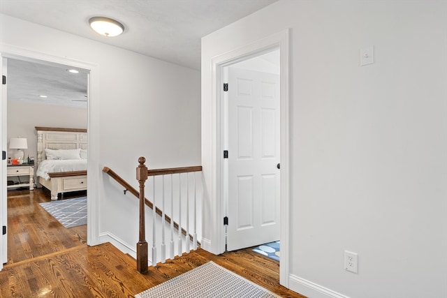 hallway featuring wood finished floors, an upstairs landing, and baseboards