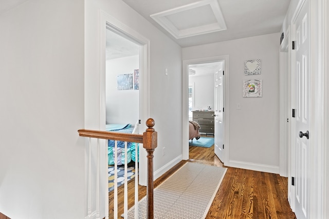 corridor featuring attic access, baseboards, and wood finished floors