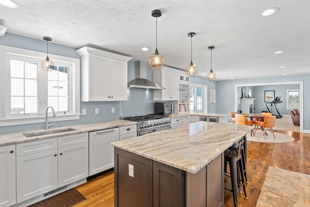 kitchen featuring range with two ovens, a wealth of natural light, a sink, dishwasher, and wall chimney exhaust hood