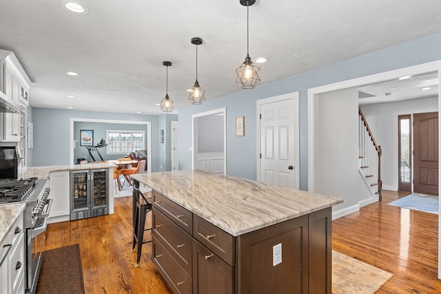 kitchen with range with two ovens, wine cooler, wood finished floors, and white cabinets