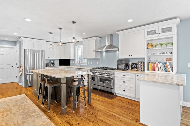 kitchen with a kitchen bar, light wood-style flooring, appliances with stainless steel finishes, white cabinets, and wall chimney exhaust hood