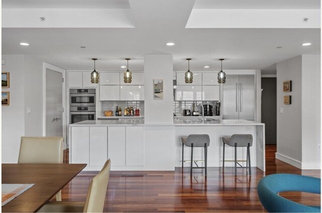 kitchen with appliances with stainless steel finishes, tasteful backsplash, dark wood-type flooring, white cabinets, and hanging light fixtures