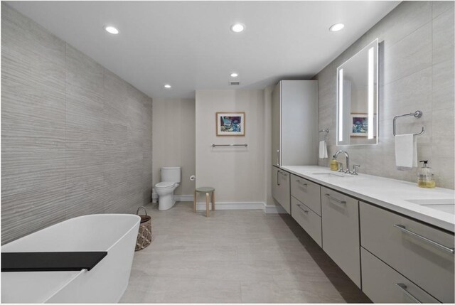 bathroom featuring vanity, a tub to relax in, toilet, and tile walls