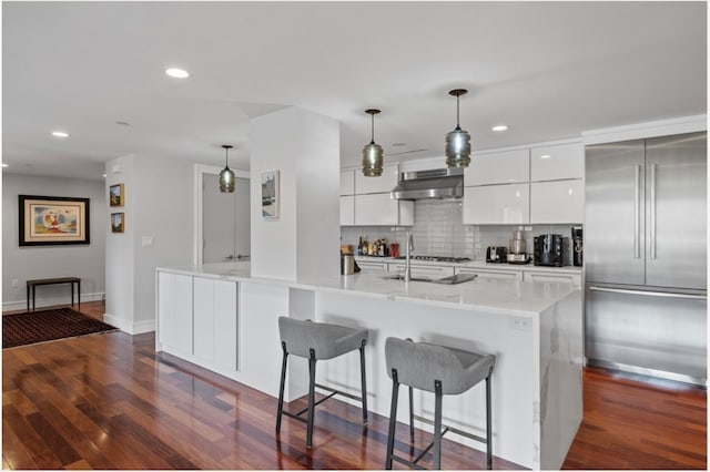 kitchen with a center island with sink, built in fridge, white cabinetry, and hanging light fixtures