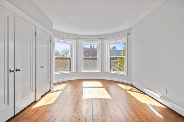 spare room featuring light hardwood / wood-style flooring, a baseboard heating unit, and a wealth of natural light