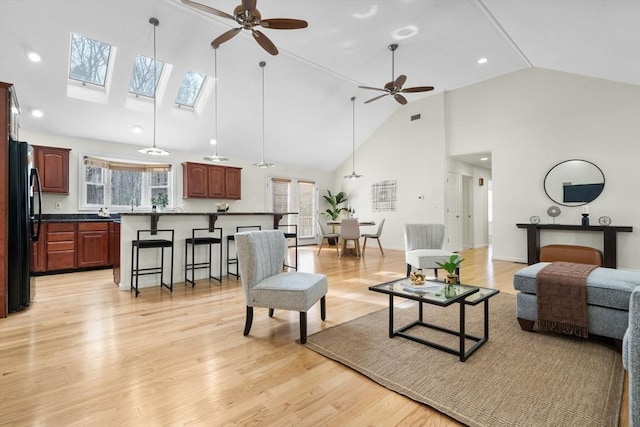 living area featuring ceiling fan, high vaulted ceiling, visible vents, baseboards, and light wood-style floors