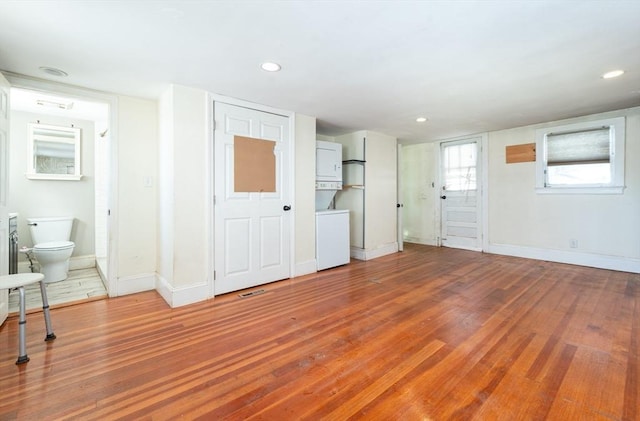 unfurnished living room featuring wood-type flooring and stacked washing maching and dryer