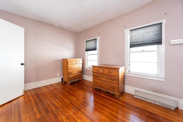 unfurnished bedroom featuring baseboard heating, dark hardwood / wood-style floors, and multiple windows