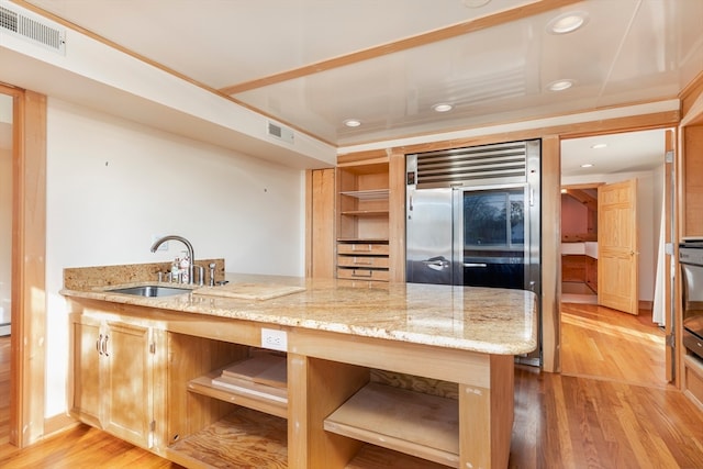 kitchen with built in fridge, sink, light hardwood / wood-style flooring, light stone counters, and kitchen peninsula