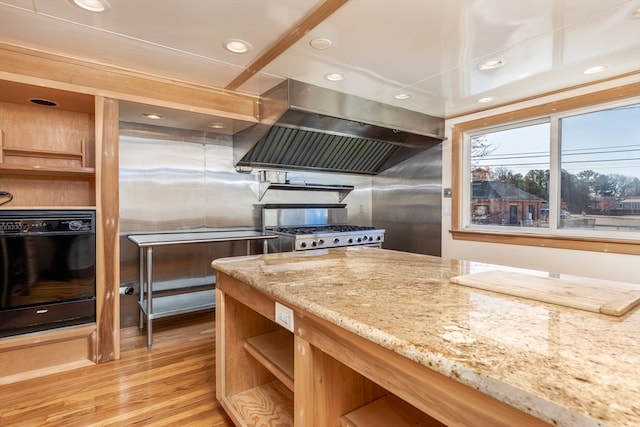 kitchen featuring stainless steel range, island range hood, light hardwood / wood-style flooring, and light stone counters