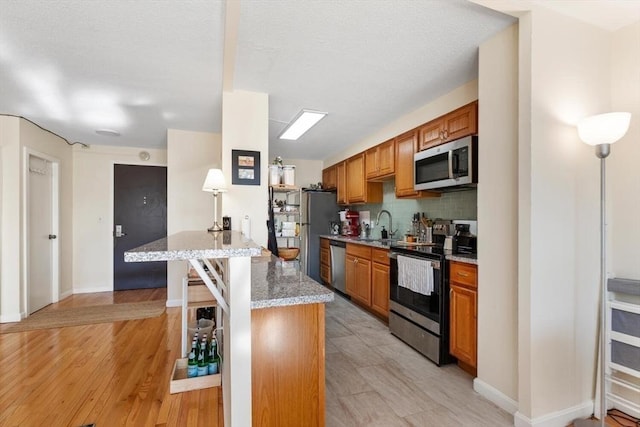 kitchen with sink, light stone counters, light wood-type flooring, appliances with stainless steel finishes, and decorative backsplash