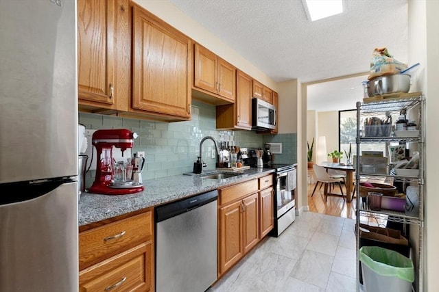 kitchen with sink, decorative backsplash, light stone counters, stainless steel appliances, and a textured ceiling