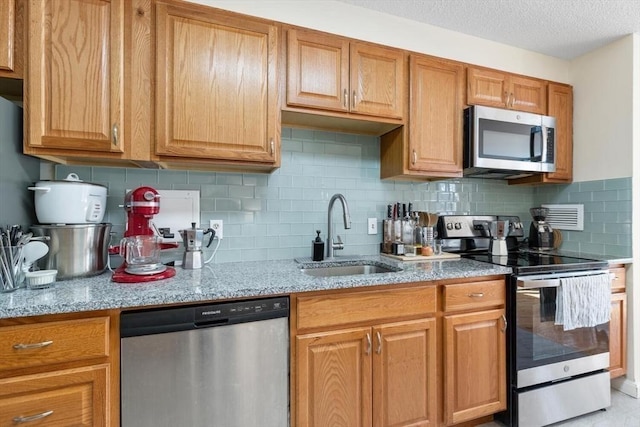 kitchen featuring sink, light stone counters, a textured ceiling, appliances with stainless steel finishes, and backsplash