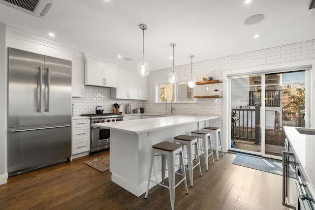 kitchen with pendant lighting, dark wood-type flooring, white cabinetry, a kitchen breakfast bar, and premium appliances