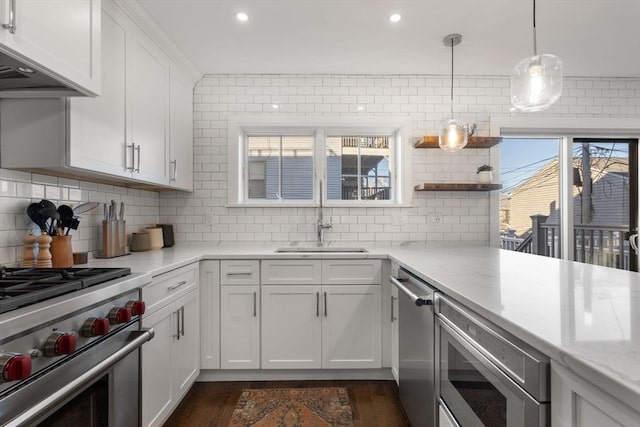 kitchen with wall chimney exhaust hood, sink, white cabinetry, decorative light fixtures, and stainless steel appliances