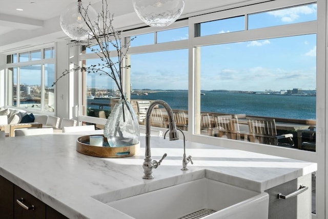 kitchen featuring light stone counters, a water view, and sink